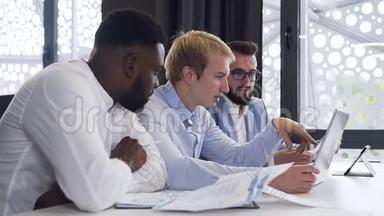 英俊的、多种族的30多岁经理在办公室里看电脑屏幕，讨论他们的商业计划